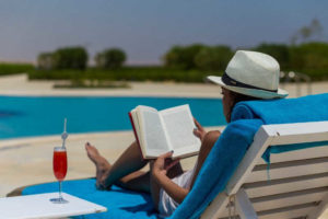female guest reading a book with a drink and pool view at byoum lakeside hotel in fayoum