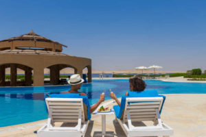 couple having a drink by the pool with a lake view at byoum lakeside hotel in fayoum